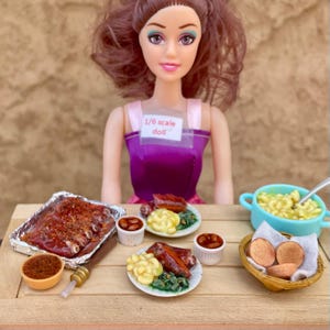 Pode incluir: Uma boneca em escala 1/6 com um top roxo atrás de um conjunto de refeição em miniatura. O conjunto inclui uma bandeja de alumínio com costelas, dois pratos com carne, macarrão e vegetais, dois copos pequenos com feijão, uma tigela azul e pães.