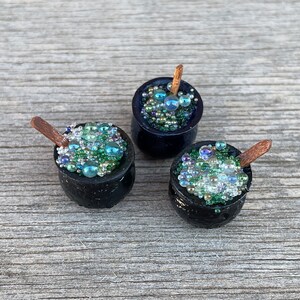 May include: Three miniature black cauldrons filled with green and blue iridescent beads, each with a small wooden stirring stick.
