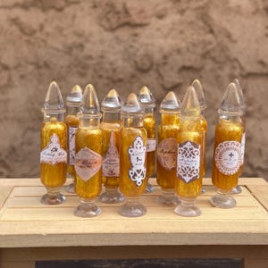 May include: A collection of miniature glass bottles with clear stoppers. The bottles are filled with a golden liquid and adorned with vintage-style labels. The labels feature ornate designs and text, adding to the antique aesthetic.
