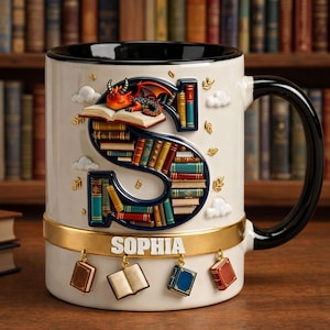 May include: A white ceramic mug with a black handle and rim, featuring a large letter "S" filled with colorful books. A small red dragon rests on an open book at the top. The name "SOPHIA" is displayed on the mug's base, with dangling book charms.
