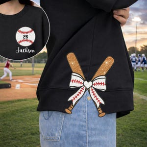 May include: Black sweatshirt with a baseball graphic on the front and back. The front features a baseball with the number 26 and the name "Jackson". The back has crossed baseball bats with a bow.
