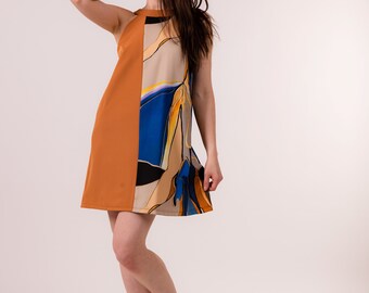 May include: A sleeveless dress with a brown and beige colour scheme. The dress has a geometric pattern with blue, yellow, and black accents. The model is wearing white trainers.
