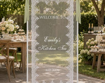 May include: A rectangular white metal frame holding a sheer white fabric panel with intricate lace borders. The panel features the white text WELCOME TO, Emily's Kitchen Tea, and 11.12.2026. Two sage green ribbons are tied to the top corners of the frame.