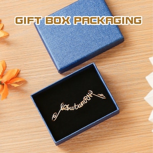 K&ouml;nnte beinhalten: Eine blaue Geschenkbox mit schwarzem Samt-Innenfutter. Die Box enth&auml;lt eine goldene Drahtskulptur mit der Aufschrift "Herbst".