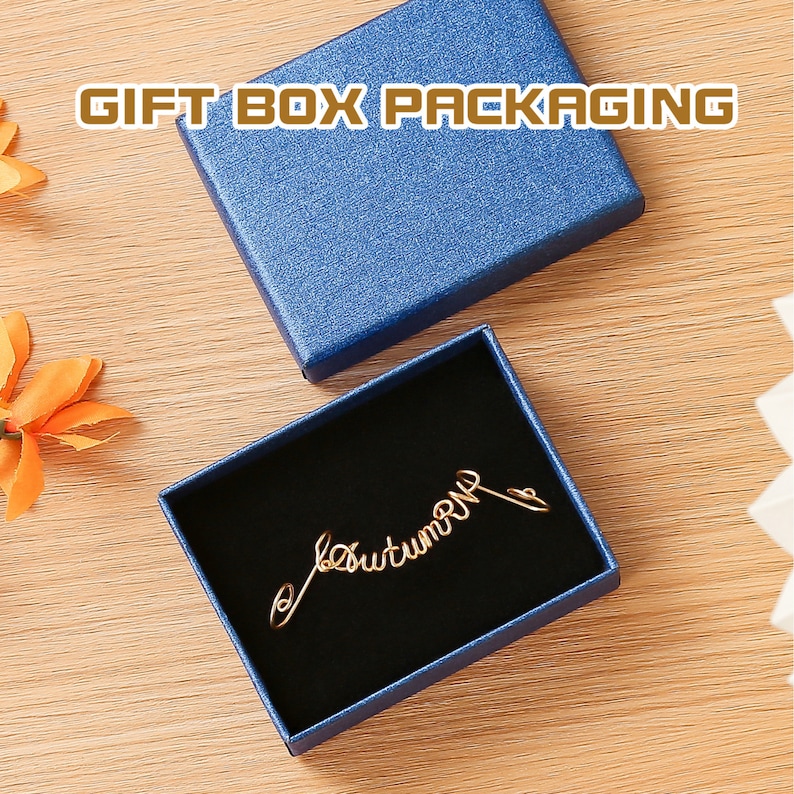 K&ouml;nnte beinhalten: Eine blaue Geschenkbox mit schwarzem Samt-Innenfutter. Die Box enth&auml;lt eine goldene Drahtskulptur mit der Aufschrift "Herbst".