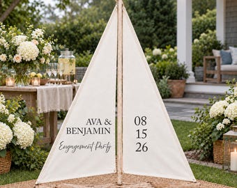 May include: A decorative sailboat sign made of driftwood and off-white fabric sails. The left sail features the black text "AVA & BENJAMIN" and "Engagement Party". The right sail displays the date "08 15 26" in black, centered on the fabric.