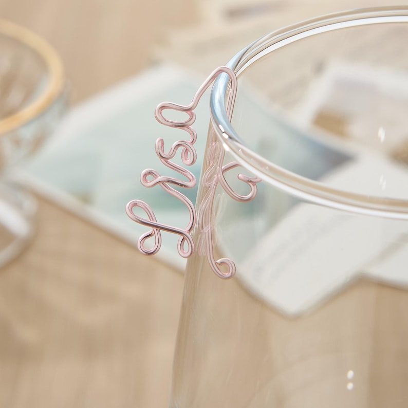 May include: A pink wire drink marker shaped like the word "Mrs."