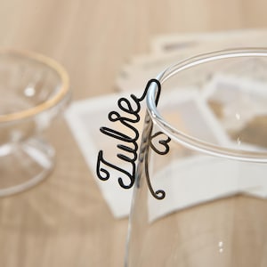 May include: A black metal wire glass charm with the word "Tulsa" written in cursive. The charm is attached to a clear glass cup.