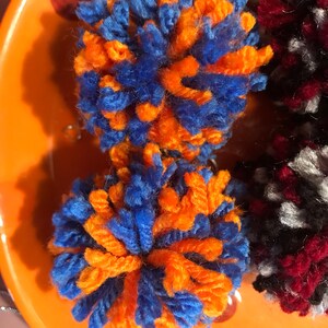 May include: Two orange and blue yarn pom-poms on an orange plate.