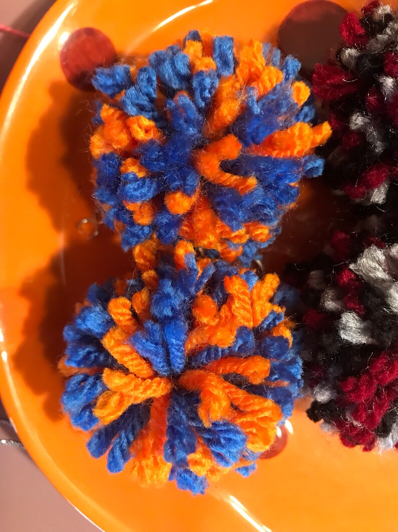 May include: Two orange and blue yarn pom-poms on an orange plate.