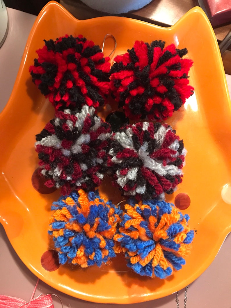 May include: Six colorful yarn pom-poms on a orange plate. The pom-poms are red and black, red and white, and orange and blue.