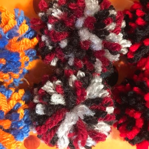 May include: Two red, black, and white pom-poms. The pom-poms are made of yarn and are fluffy.