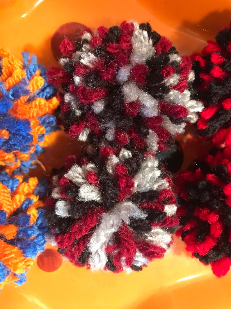 May include: Two red, black, and white pom-poms. The pom-poms are made of yarn and are fluffy.