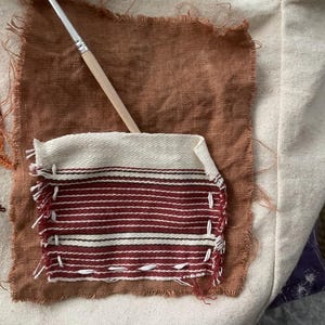 May include: Close-up of a canvas tote bag with a patch of brown fabric and a smaller patch with red and white stripes. A paintbrush rests on the patches. The bag is made of natural-colored canvas.