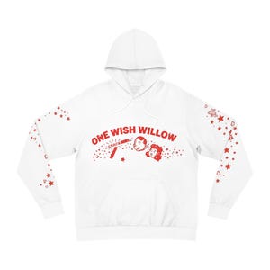 Puede incluir: Una sudadera con capucha blanca que presenta un estampado gráfico rojo en el pecho con el texto ONE WISH WILLOW, junto a una ilustración de dos rostros y un cracker. Las mangas están decoradas con un patrón de pequeñas estrellas y corazones.