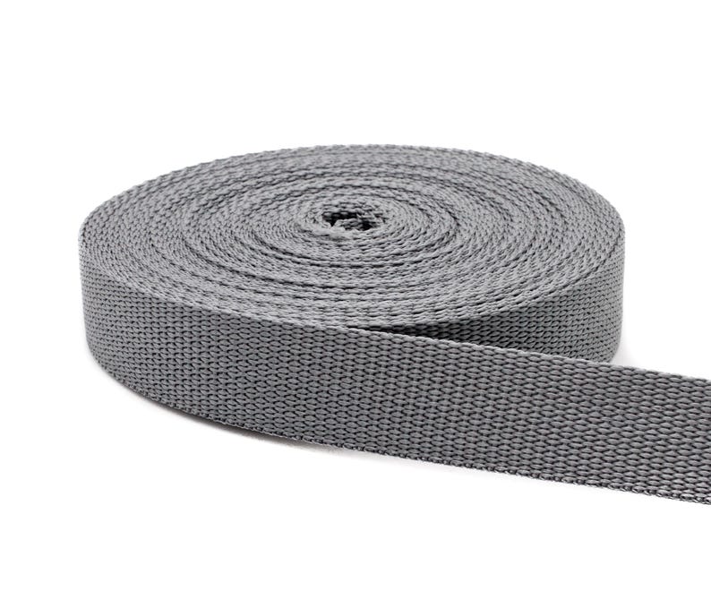 May include: A roll of gray webbing, a type of strong, woven fabric often used for straps, belts, and other applications.