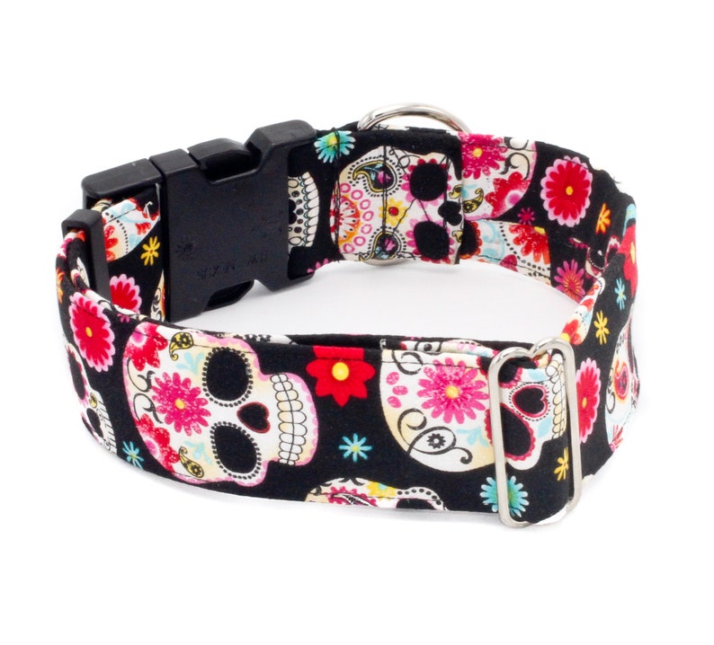 May include: A black dog collar with a colorful sugar skull pattern. The collar has a black plastic buckle and a silver metal D-ring.