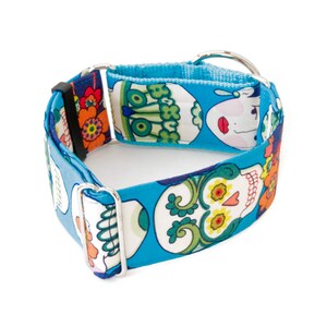 May include: A blue dog collar with a repeating pattern of white sugar skulls, flowers, and green swirls. The collar has a metal D-ring and a black plastic buckle. The interior of the collar is a lighter blue fabric.