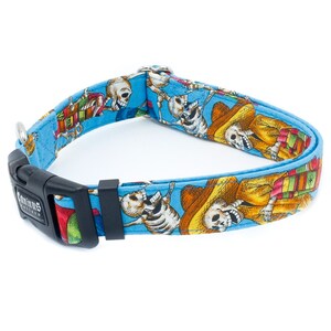 Pode incluir: Uma coleira de cachorro azul com um padr&atilde;o colorido de esqueletos usando sombreros e tocando instrumentos musicais. A coleira tem uma fivela preta com o texto "Canine Styles" nela.