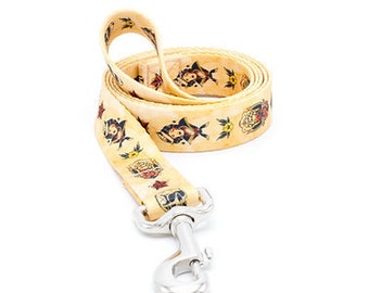 Op de afbeelding: Een gele hondenriem met een zilveren clip. De riem is versierd met een patroon van kleurrijke tatoeages.