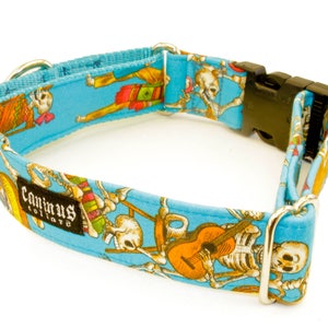 Pode incluir: Uma coleira de c&atilde;o azul com um design colorido de esqueleto e guitarra. A coleira tem uma fivela prateada e o texto "Caninus Collars" est&aacute; impresso na coleira.