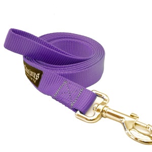 May include: A coiled purple dog leash with a gold-colored metal clasp. The leash is made of a durable woven material and features a label with white text. The leash is designed for pet owners to safely walk their dogs.