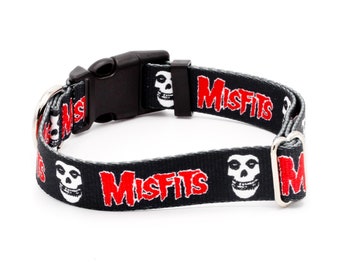 May include: Black dog collar with a repeating pattern of the Misfits logo and a skull. The collar has a black plastic buckle and a silver metal D-ring.