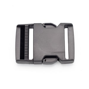 Puede incluir: Hebilla de plástico negro con mecanismo de liberación lateral. La hebilla tiene un acabado liso y mate.