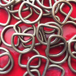 May include: A pile of silver-toned metal D-rings on a red surface. The rings are about 1 inch in diameter.