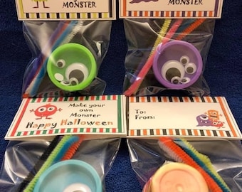 May include: Four clear plastic bags with colorful monster-themed Halloween craft kits. Each bag contains a small container of play dough, googly eyes, pipe cleaners, and a card that says "Happy Halloween, Make your own monster".