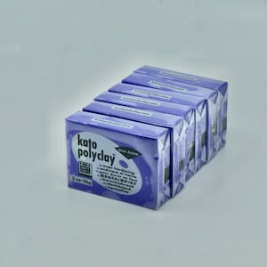 May include: Five packages of purple oven-bake clay, each labeled "Kato Polyclay" with the brand name "Van Aken" and the text "2 oz - 56g". The packaging also includes instructions for oven hardening in various languages.