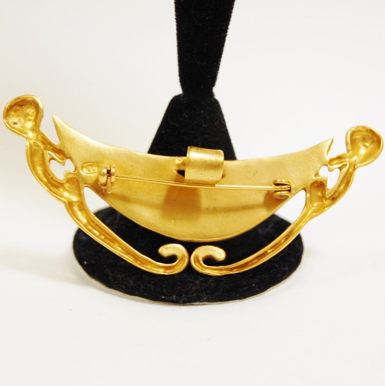 May include: Gold-toned crescent moon brooch with intricate details and a pin closure on the back.