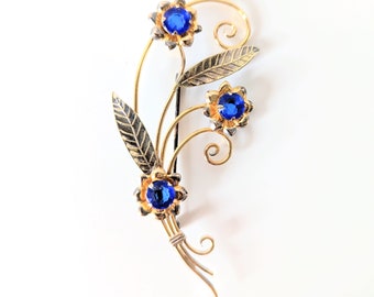 May include: A gold-toned brooch with three blue rhinestone flowers and a leaf design.