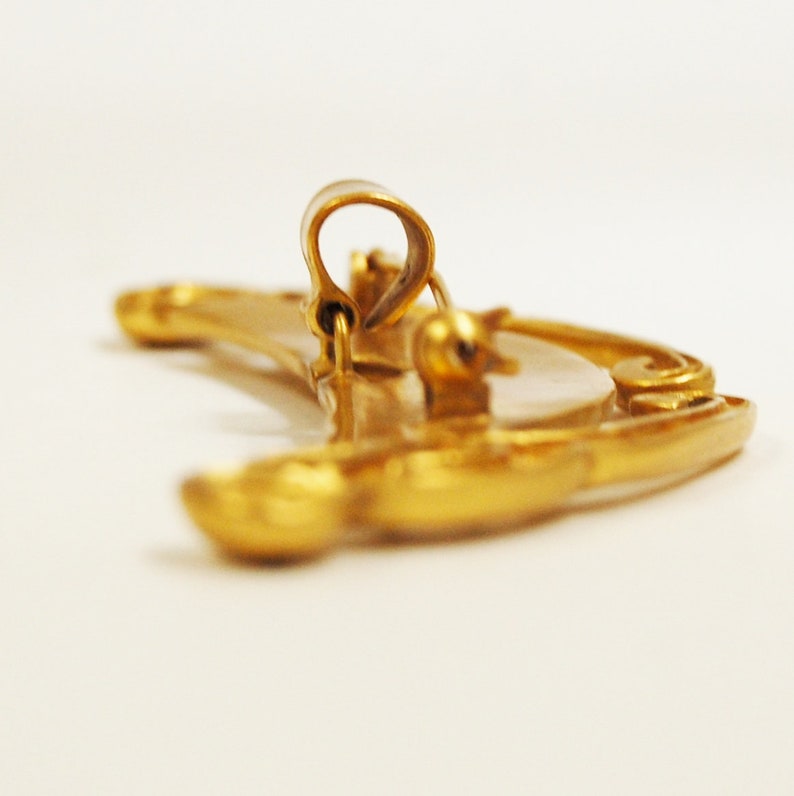 May include: A gold crescent moon shaped brooch with a decorative design. The brooch has a pin and catch closure on the back.