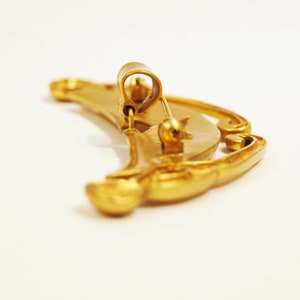 May include: A gold-toned crescent moon brooch with intricate details and a pin closure.
