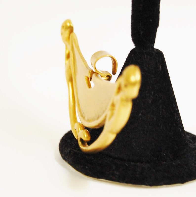 May include: A gold-toned metal pendant in the shape of a crescent moon with intricate details. The pendant is on a black velvet display stand.