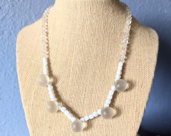 May include: A white beaded necklace with five clear glass beads. The necklace is on a white mannequin.