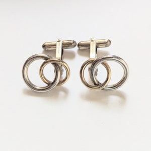 May include: A pair of silver cufflinks with a gold ring design. The cufflinks are marked "925 Sterling".