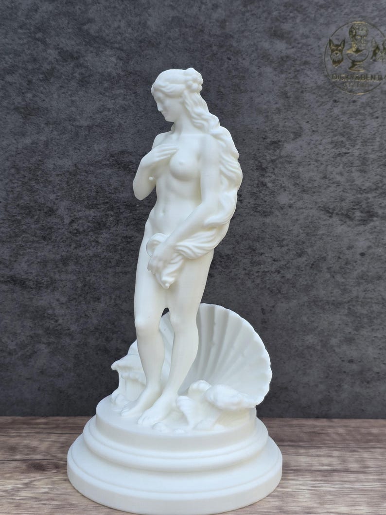May include: A white matte sculpture of a standing figure with long flowing hair, partially covering the chest with one hand and holding a draped cloth. The figure stands on a circular base in front of a large, open seashell, rendered in solid white.
