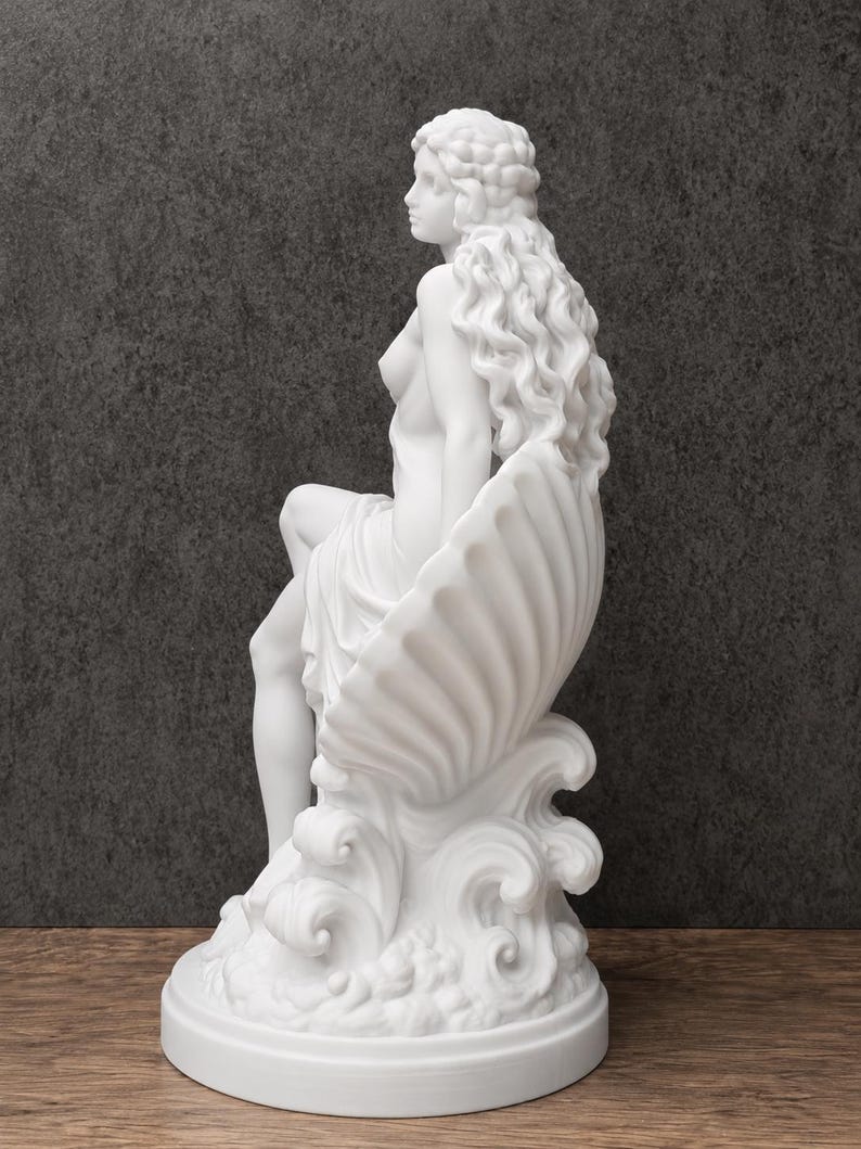 K&ouml;nnte beinhalten: Eine wei&szlig;e, matte Skulptur einer Figur mit langem, flie&szlig;endem, welligem Haar, die in einer gro&szlig;en, gerippten Muschel sitzt. Die Figur ist auf stilisierten, wirbelnden Wellen positioniert, die einen kreisf&ouml;rmigen Sockel bilden.