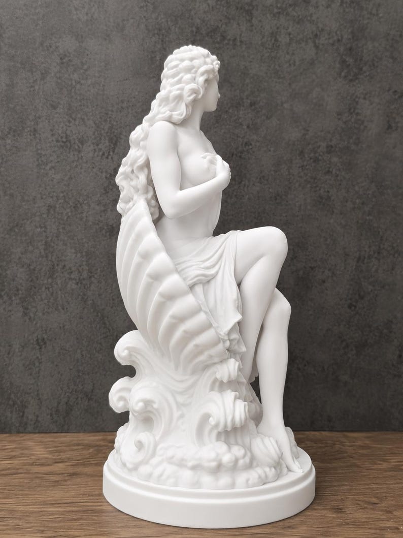 K&ouml;nnte beinhalten: Eine wei&szlig;e, matte Skulptur einer Figur mit langem, flie&szlig;endem Haar, die in einer gro&szlig;en Muschel sitzt, welche auf stilisierten Meereswellen ruht. Die Figur ist im Profil dargestellt, eine Hand an der Brust und Stoff &uuml;ber die Beine drapiert.