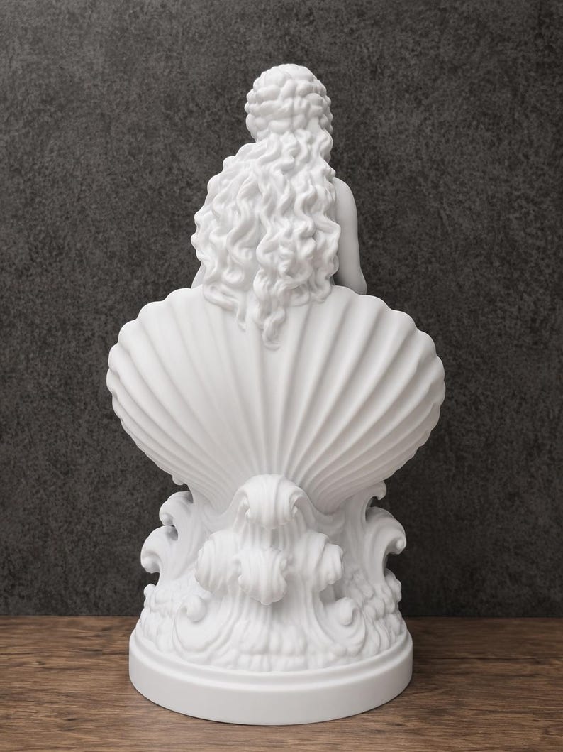 K&ouml;nnte beinhalten: Eine mattwei&szlig;e Skulptur, die eine Figur mit langem, flie&szlig;endem, welligem Haar zeigt, die in einer gro&szlig;en, vertikal gerippten Muschel sitzt. Der Sockel der Skulptur weist stilisierte, wirbelnde Wellenmuster auf, die ein einheitliches Design bilden.