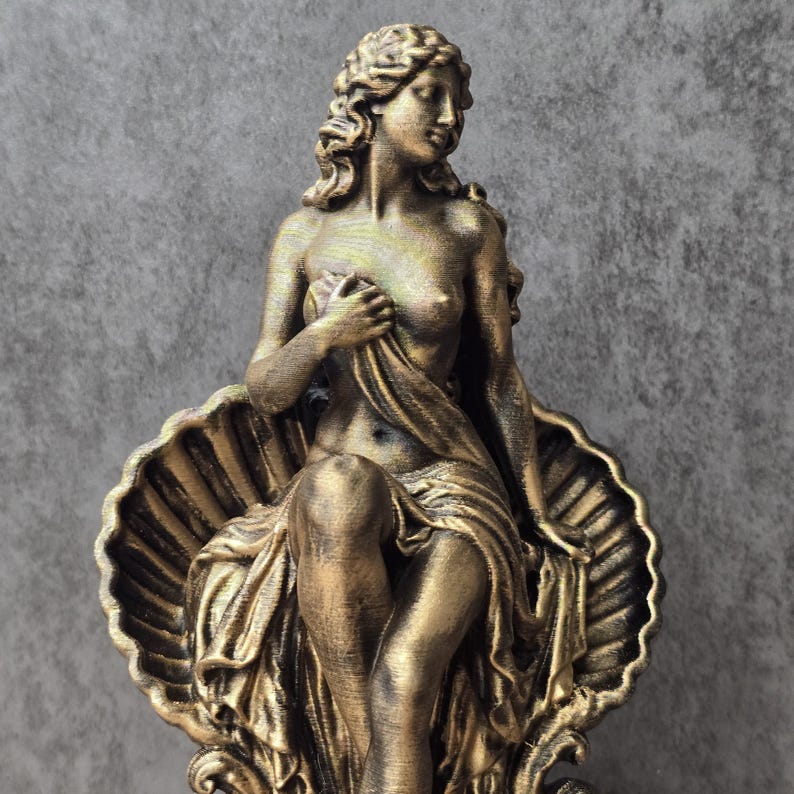 K&ouml;nnte beinhalten: Eine bronzefarbene Statue einer Figur mit langem, welligem Haar, die in einer gro&szlig;en, detaillierten Jakobsmuschel sitzt. Die Figur ist teilweise mit Stoff bedeckt, der den Unterk&ouml;rper verh&uuml;llt und &uuml;ber der Brust gehalten wird.