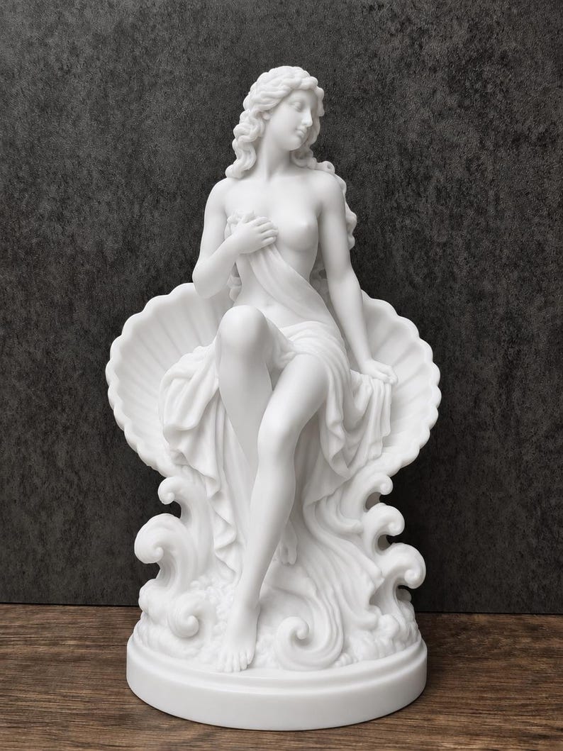 K&ouml;nnte beinhalten: Eine wei&szlig;e, matte Skulptur einer Figur mit langem, flie&szlig;endem Haar, die in einer gro&szlig;en, muschelf&ouml;rmigen Schale sitzt. Die Figur ist teilweise mit Stoff drapiert und ruht auf stilisierten Wellen auf einem runden Sockel.