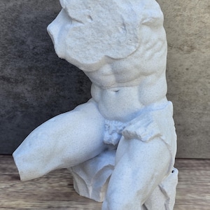 May include: A white, sculpted torso statue with detailed musculature. The sculpture depicts a male figure, with arms bent and legs partially visible. The statue is made of a speckled, textured material, and is set against a neutral background.