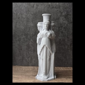 Può includere: Un vaso scultoreo bianco opaco a tre lati raffigurante tre figure identiche con vesti drappeggiate disposte schiena contro schiena. La colonna centrale si eleva sopra le figure, formando un'apertura cilindrica sulla sommità.