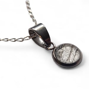 Puede incluir: Un collar de cadena de plata con un colgante redondo que presenta una rebanada de meteorito negro y blanco.