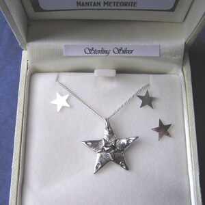 Puede incluir: Un conjunto de collar y pendientes de plata con un colgante de estrella de cinco puntas y pendientes a juego. El colgante es texturizado y tiene una forma ligeramente irregular. El conjunto se presenta en una caja blanca con las palabras "Nantan Meteorite" y "Sterling Silver" impresas en la tapa.