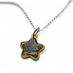 May include: A silver chain necklace with a gold star-shaped pendant. The pendant contains a piece of pyrite, a metallic mineral with a silvery-grey colour.