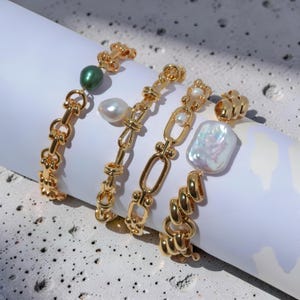 May include: Four gold-toned bracelets with various designs. One features a green pearl, another a white pearl, and a third a large, iridescent pearl. The bracelets have different link styles, including chain and knot designs. The jewelry is displayed on a white surface.